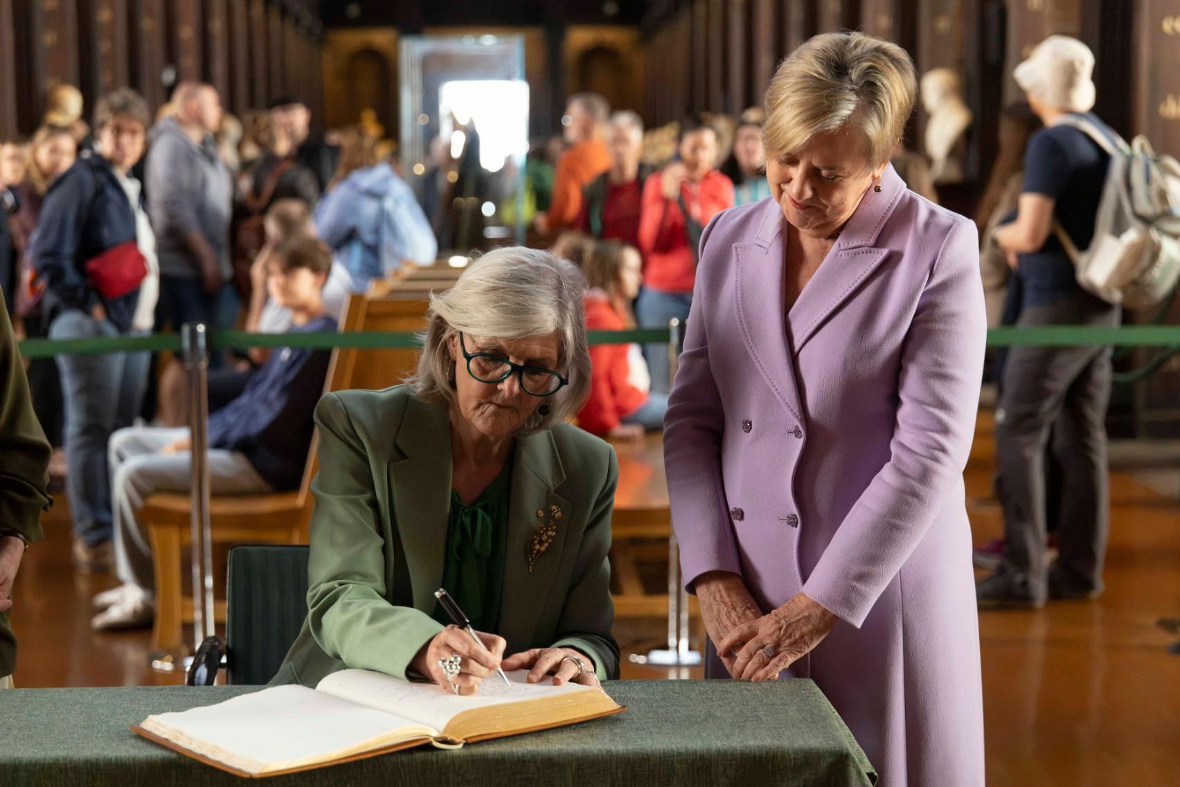 A woman looks on as another woman signs a book