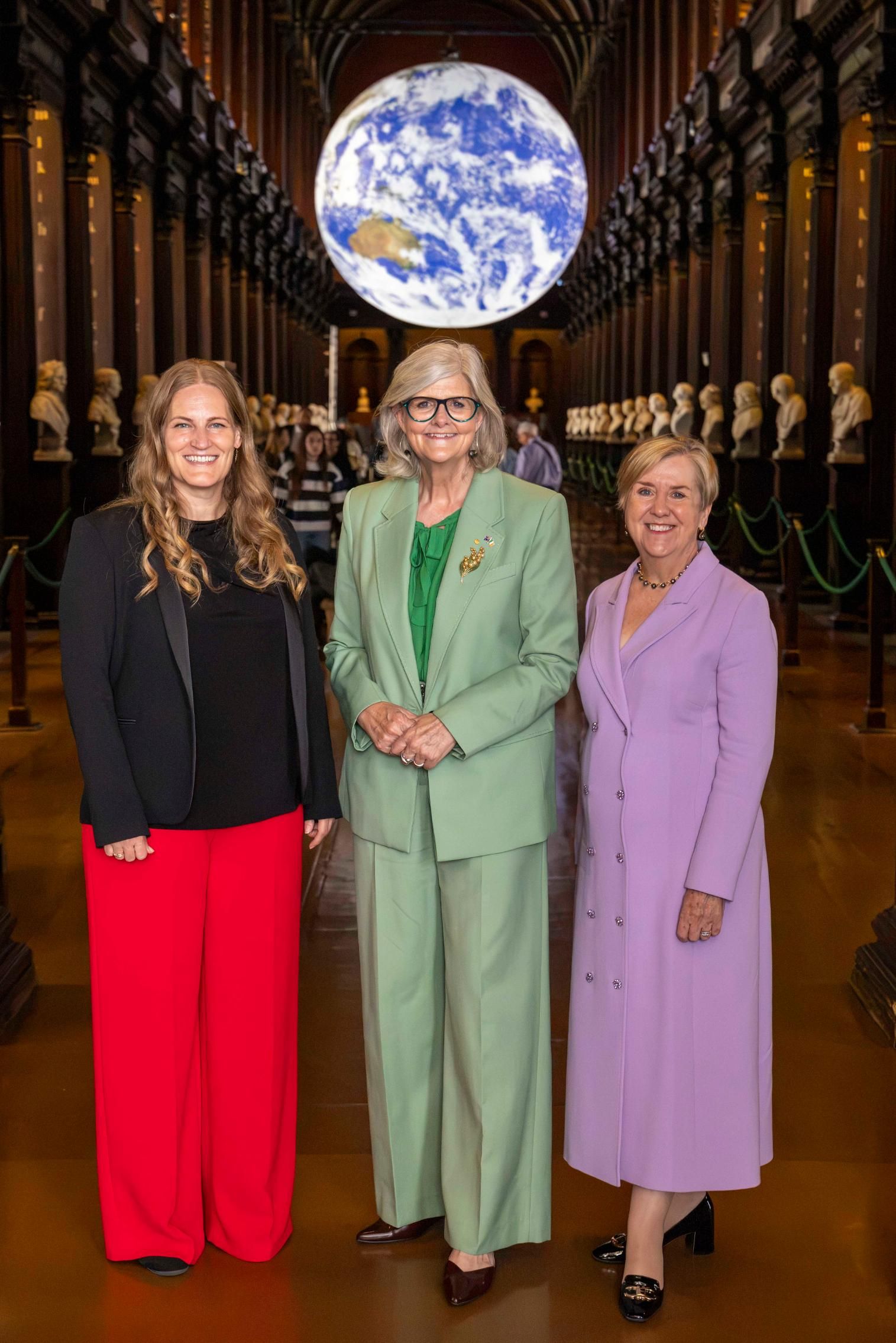 Three women stand together in the Long Room of Trinity College Dublin