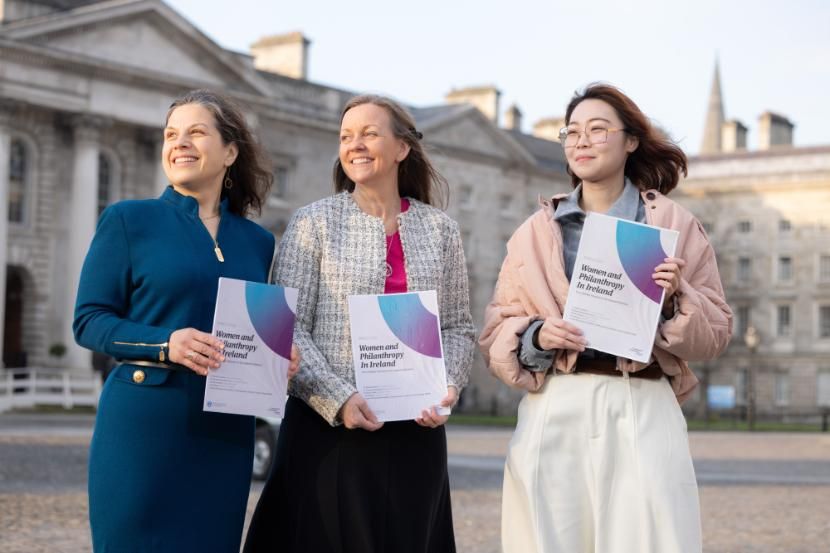 Three women standing in Trinity's Front Square holding a report