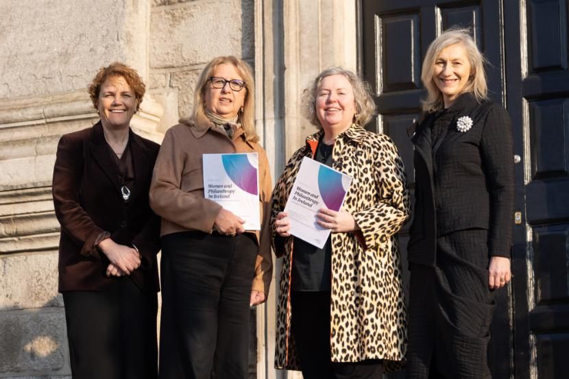 Four women sanding outside Trinity's Dining Hall with two holding a report