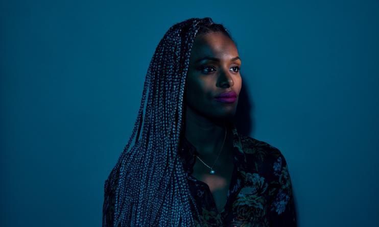 Professor Abeba Birhane, with braided hair, standing in front of a dark blue background.