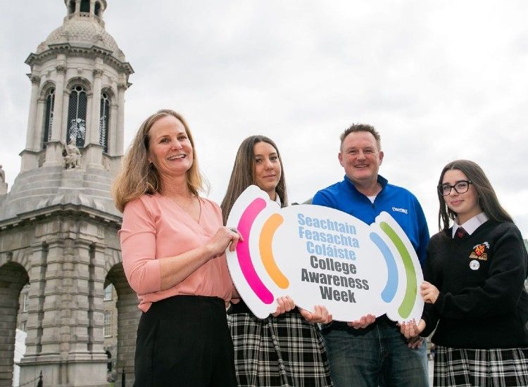 four people hold a sign in front of Bell Tower