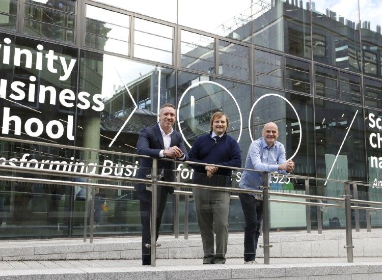 Three men pose outside modern building