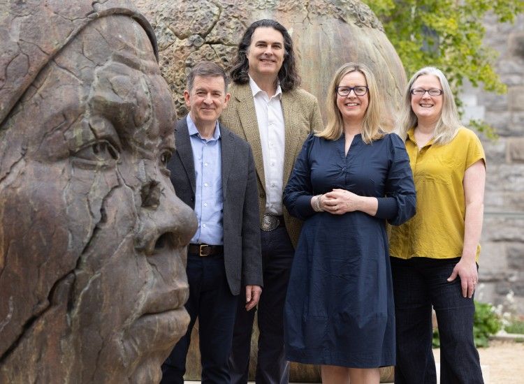 Four people pose beside sculpture