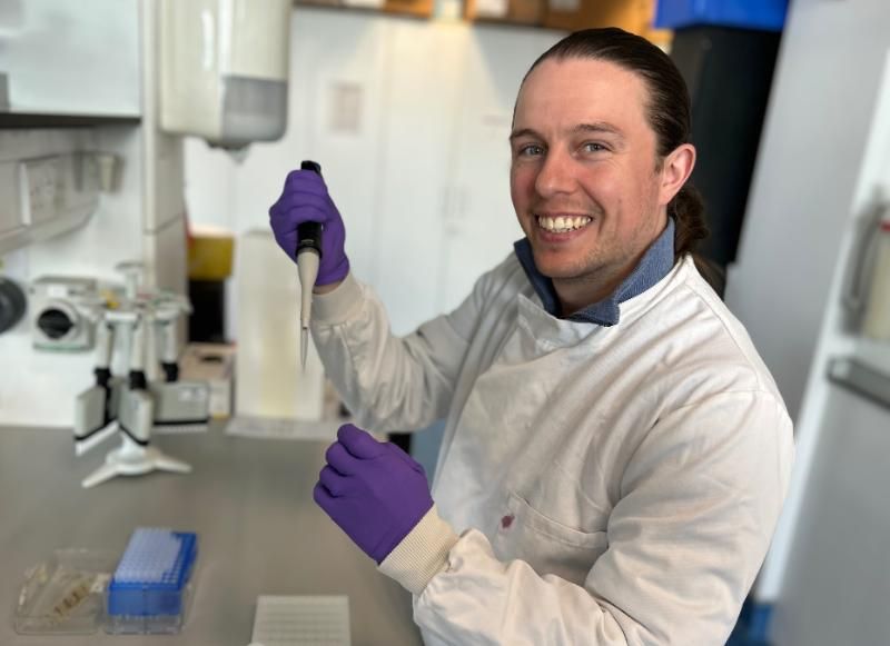Dr Dylan Ryan, wearing a lab coat, pipettes chemicals in a laboratory.