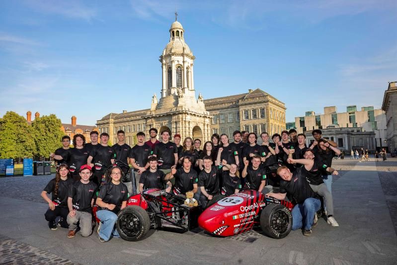 Many of the Formula Trinity student team with their formula race car, Bruce, in Front Square with the campanile behind.