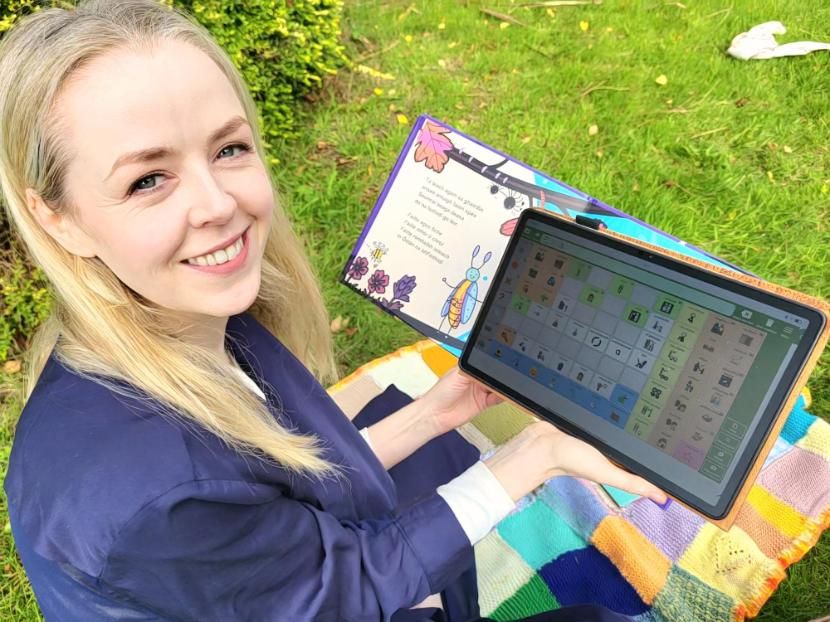 A woman holds a children's book and a tablet