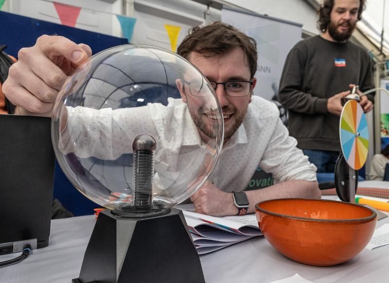 A man in a white lab coat looks through a prism with a bolt of electricity.
