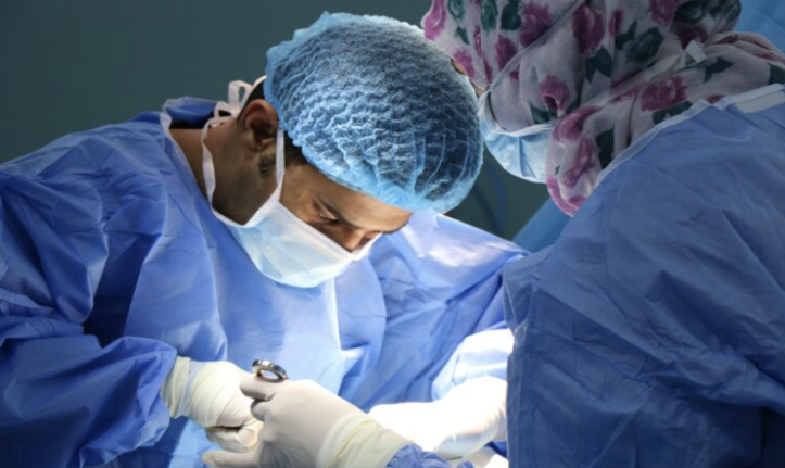 A surgeon performing surgery dressed in a blue medical scrubs.