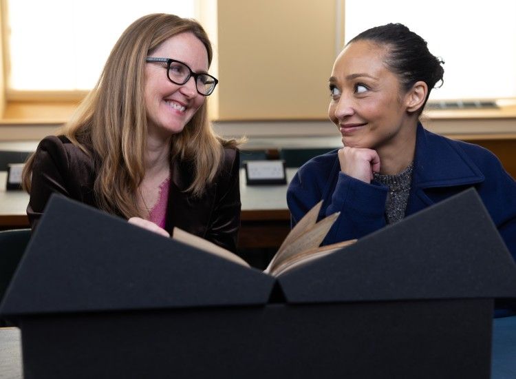 Two women smile as theye examine a manuscript