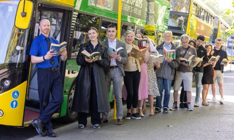 A group of people reading books in front of a double decker bus