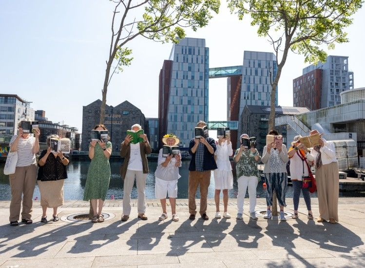 Group of people holding up books on a sunny day