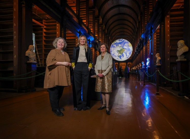 Three women pose in the Old Library at Trinity