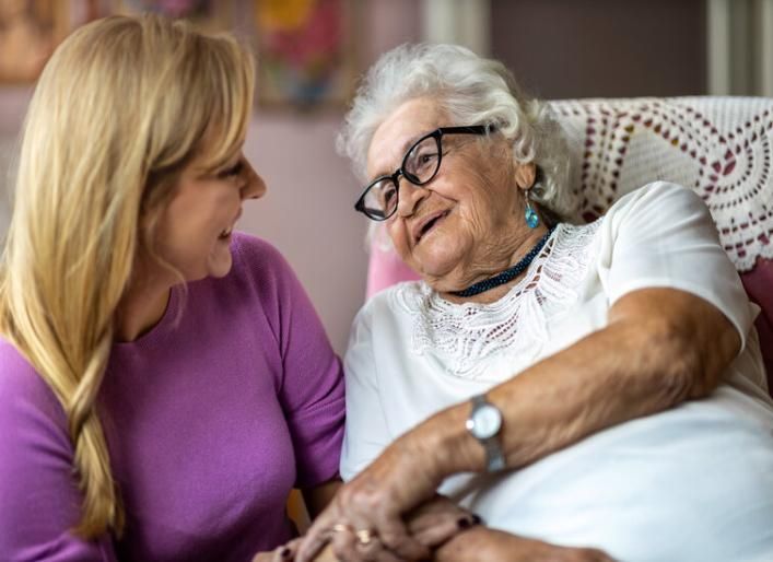 An older woman sits with a care-giver, holding hands