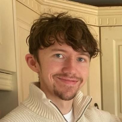 Student with short brown hair and facial hair smiling at camera.