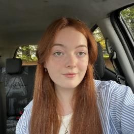 student with red hair smiling at a camera