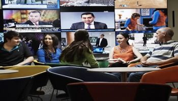 A group of students talking with tv screens on in the background